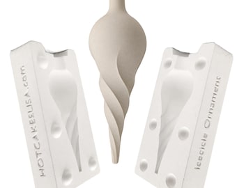 May include: A beige, spiral-shaped icicle ornament positioned between two white plaster mold halves. The left mold is embossed with the text HOTCAKESUSA.COM and the right mold is embossed with the text ICICICLE ORNAMENTS.