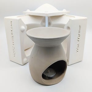 May include: A white ceramic wax warmer with a round opening for a tea light candle. The warmer is made in a mold, which is also shown in the image. The mold is made of white silicone and has the words "HOTCAKEUSA.com" and "Wax Warmer" printed on it.