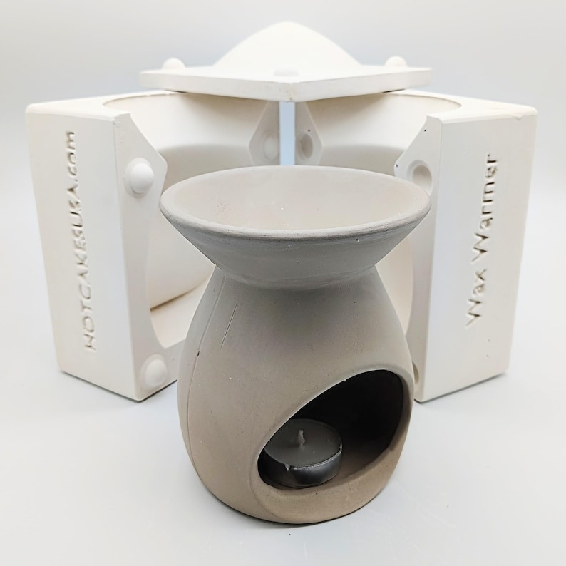 May include: A white ceramic wax warmer with a round opening for a tea light candle. The warmer is made in a mold, which is also shown in the image. The mold is made of white silicone and has the words "HOTCAKEUSA.com" and "Wax Warmer" printed on it.