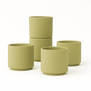 May include: Five olive-green ceramic cups. The cups are cylindrical with a slightly flared base. Two cups are stacked, and the others are arranged around them. The cups have a matte finish and a simple, modern design.