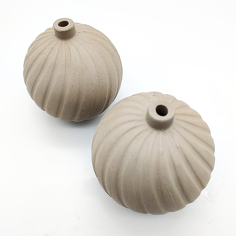 May include: Two brown ceramic vases with a ribbed design. The vases are round and have a small opening at the top.