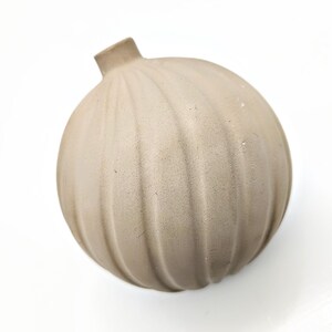 May include: A light brown ceramic vase with a round, ribbed design. The vase has a small opening at the top.