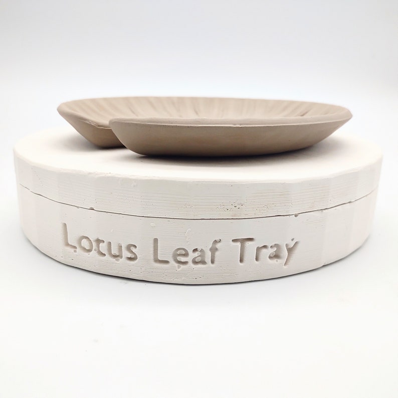 May include: A white ceramic tray with the words "Lotus Leaf Tray" embossed on the side. The tray has a matching beige ceramic lotus leaf dish on top.