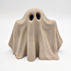 May include: A beige ceramic ghost figurine with two black eye holes.