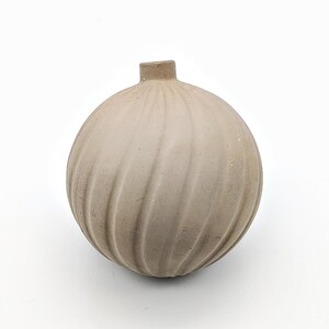 May include: A small, round, light brown ceramic vase with a textured, swirl design.