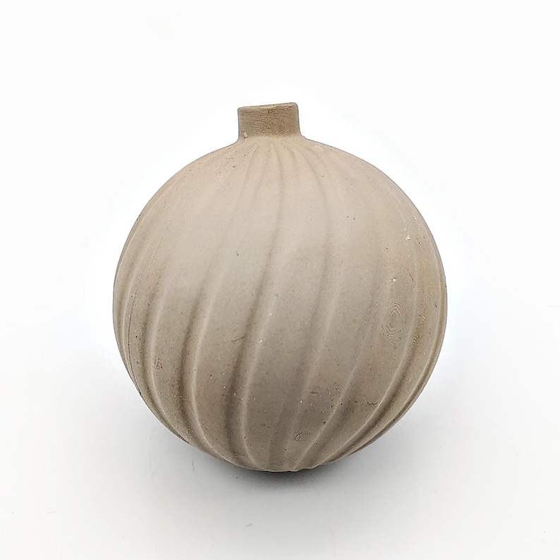 May include: A small, round, light brown ceramic vase with a textured, swirl design.