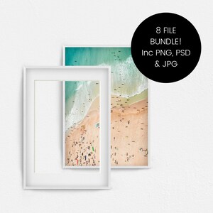 May include: Two white picture frames containing a beach scene. The beach scene is an aerial view of a beach with people on it. The water is turquoise and the sand is white. The frames are on a white wall.