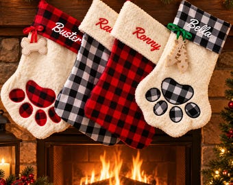 May include: Four personalized Christmas stockings shaped like animal paws. Two feature red and black buffalo plaid cuffs with names Buster and Ronny, while two have black and white plaid cuffs with names Bella and Ray. Each has a plush white body.