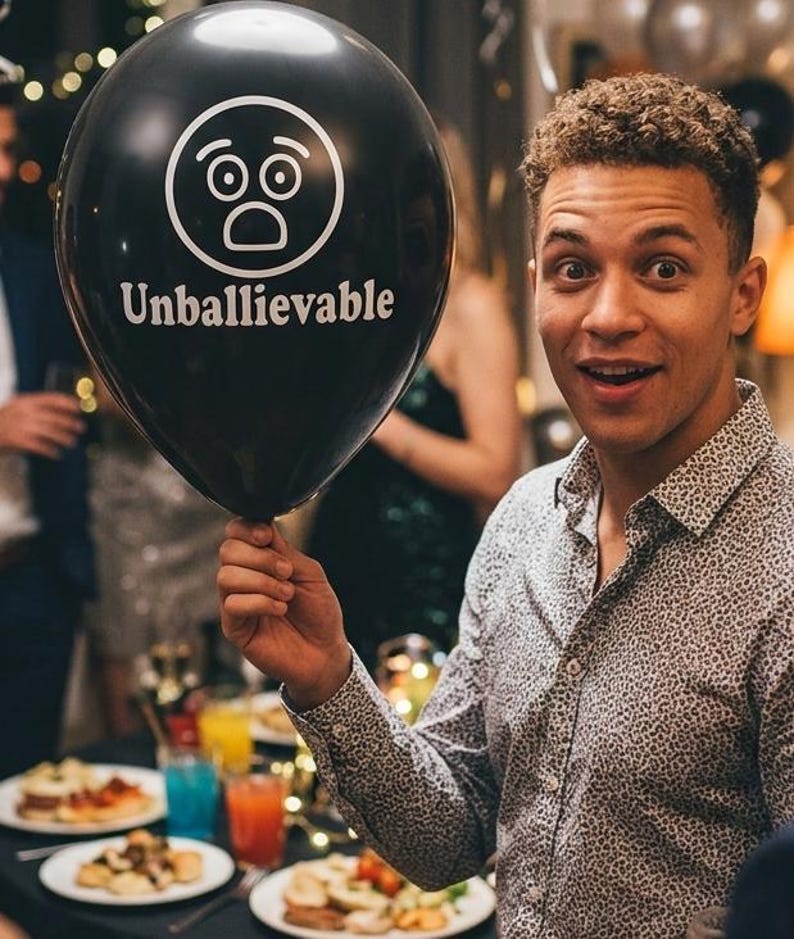 May include: A black balloon featuring a white graphic of a shocked face icon and the text Unballievable printed in white. The balloon is round and inflated, displaying a clear, bold design that stands out against the dark, glossy surface of the latex.