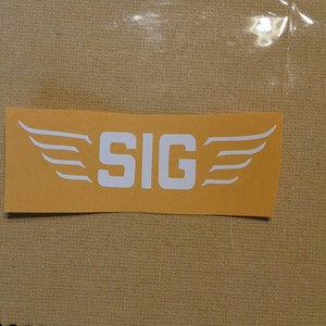 May include: A yellow sticker with white wings and the word "SIG" in white letters.