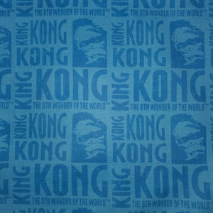 May include: A blue fabric featuring a repeating pattern of "KONG" text and a gorilla face. The phrase "THE 8TH WONDER OF THE WORLD" is also printed on the fabric. The design is a repeating pattern.