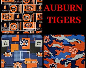 May include: Three different fabric patterns featuring the Auburn Tigers logo. The first pattern is a blue and orange repeating pattern with the Auburn Tigers logo and the words "Auburn University" and "Auburn Tigers". The second pattern is a blue and orange geometric pattern with the Auburn Tigers logo and the words "Auburn" and "Tigers". The third pattern is a camouflage pattern in blue, orange, and white with the Auburn Tigers logo.