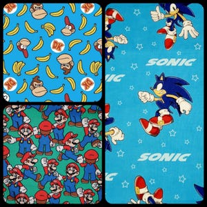 May include: Four different fabric patterns featuring popular video game characters. The first pattern is blue with yellow bananas and a cartoon monkey. The second pattern is blue with white stars and the text "SONIC". The third pattern is green with a repeating pattern of Mario characters. The fourth pattern is blue with white stars and the text "SONIC".