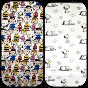 Könnte beinhalten: Zwei Stoffmuster, eines mit einem sich wiederholenden Muster von Peanuts-Charakteren, darunter Charlie Brown, Snoopy, Lucy und Linus, und das andere mit einem sich wiederholenden Muster von schlafenden Snoopy und Pfotenabdrücken.