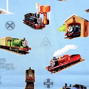 May include: Light blue fabric patterned with cartoon train illustrations. The trains are in various colours, including blue, green, and red, with smiling faces. The fabric also features railway signs and a water tower.