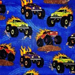 May include: A repeating pattern of colorful monster trucks with flames on a blue background. The trucks are in various colors, including green, purple, and red, with large black tires. The design includes brown dirt and white splashes.