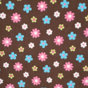 May include: Brown fabric with a repeating pattern of colorful flowers. The flowers are in shades of pink, blue, white, and green. The fabric is likely used for crafts or sewing projects.