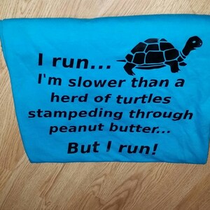 May include: A folded turquoise t-shirt with the text "I run... I'm slower than a herd of turtles stampeding through peanut butter... But I run!" and a black turtle graphic.