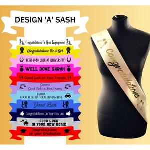 May include: A gold satin sash with the word "Congratulations" printed in gold lettering. The sash is displayed on a black mannequin. The image also shows a variety of colourful sashes with different messages printed on them.