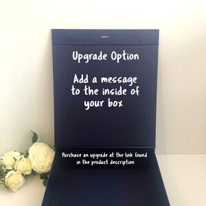 May include: A navy blue gift box with a white lid. The lid is open and the inside of the box is visible. The lid has the text "Upgrade Option" and "Add a message to the inside of your box". The bottom of the box has the text "Purchase an upgrade at the link found in the product description".