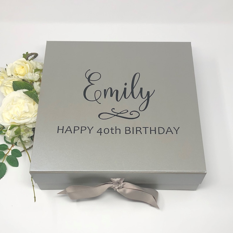 May include: A silver gift box with a gray ribbon. The box has the text "Emily Happy 40th Birthday" printed on the top.