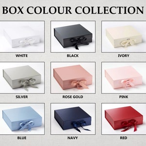 May include: A collection of nine gift boxes in various colors, including white, black, ivory, silver, rose gold, pink, blue, navy, and red. Each box has a satin ribbon tied around it.