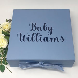 May include: A light blue gift box with a blue ribbon tied around it. The box has the text "Baby Williams" printed on the top in black.