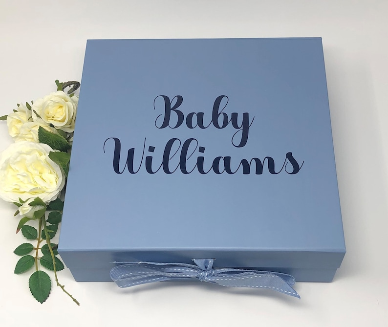 May include: A light blue gift box with a blue ribbon tied around it. The box has the text "Baby Williams" printed on the top in black.
