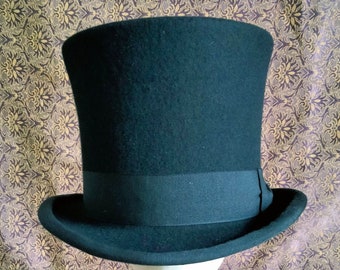 Puede incluir: Un sombrero de copa negro con una cinta negra. El sombrero está sentado en una cabeza de maniquí blanca.
