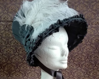 Op de afbeelding: Een donkergrijze hoed met een gerimpelde rand en witte veren. De hoed wordt getoond op een witte mannequinhoofd met een donkergrijs lint om de nek. De hoed is een vintage stijl.