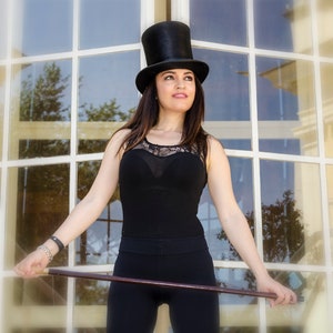 Puede incluir: Una mujer con un top negro y pantalones negros con un sombrero de copa negro. Est&aacute; sosteniendo un bast&oacute;n de madera.