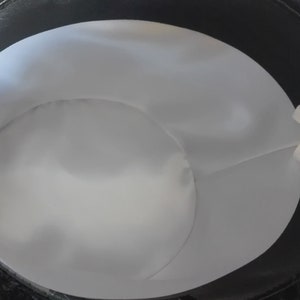 Puede incluir: Un sombrero de copa negro con forro blanco y una cinta blanca atada en el interior.