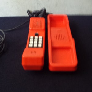 May include: A bright red vintage rotary phone with a matching red cradle. The phone has a black keypad and a black speaker.