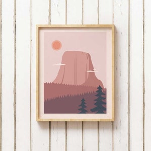May include: A framed print of a pink mountain with a red sun in the sky. The mountain is surrounded by a forest of dark green trees. The print has a light pink background.