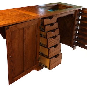 May include: A wooden sewing table with a drop-down leaf, six drawers, and a cabinet door. The table is made of dark wood with a natural finish.