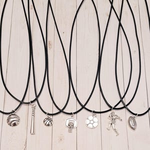 May include: Eight necklaces with black cords and silver sport-themed pendants. The pendants include a baseball, bat, basketball, basketball hoop, football, rugby ball, and a rugby player.
