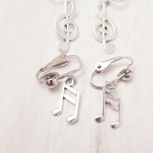 May include: A pair of silver clip-on earrings with a treble clef charm and a pair of silver clip-on earrings with a musical note charm.