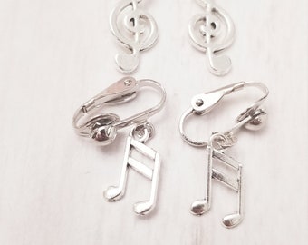 Peut inclure: Une paire de boucles d'oreilles clips argentées avec un charme de clé de sol et une paire de boucles d'oreilles clips argentées avec un charme de note de musique.