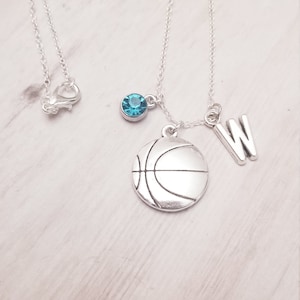 Peut inclure: Collier en argent avec un pendentif en forme de ballon de basket, un pendentif en cristal bleu et un pendentif en forme de lettre W.