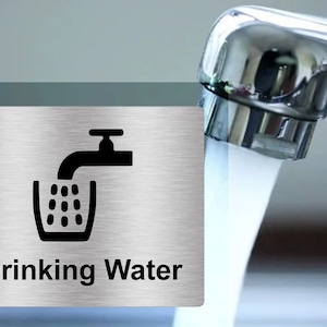 Peut inclure: Une plaque en acier inoxydable avec une silhouette noire d'un robinet versant de l'eau dans un verre. La plaque indique "Eau potable".