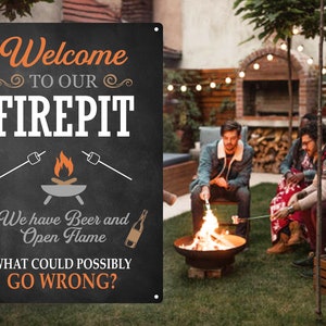 May include: A black metal sign with white text that reads "Welcome to our Firepit. We have Beer and Open Flame. What could possibly go wrong?" The sign is hanging on a wall in a garden with a fire pit and people toasting marshmallows.