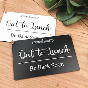 May include: Two signs, one black and one white, with the text "Out to Lunch" and "Be Back Soon" in a decorative script font. The signs are hanging from twine.