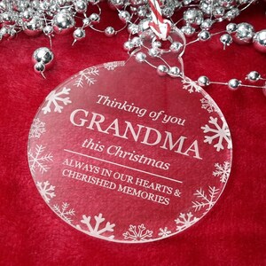 May include: Clear glass Christmas bauble with white snowflakes and the text "Thinking of you GRANDMA this Christmas ALWAYS IN OUR HEARTS & CHERISHED MEMORIES".