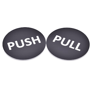 Peut inclure: Deux panneaux ronds noirs avec du texte blanc. Un panneau indique "PUSH" et l'autre "PULL".