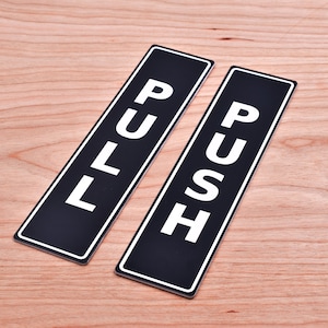 May include: Two black rectangular signs with white text. One sign says "PULL" and the other says "PUSH".