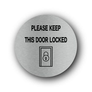 Può includere: Un cartello rotondo in metallo spazzolato con la scritta "PLEASE KEEP THIS DOOR LOCKED" in nero, sopra un disegno a tratto nero di una porta con un lucchetto. Il cartello ha un effetto ombra.