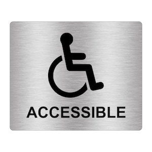 Może przedstawiać: Srebrny metalowy znak z czarnym symbolem wózka inwalidzkiego i napisem "ACCESSIBLE" w czarnym kolorze.