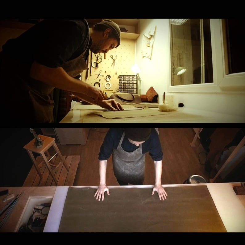 May include: A person working on a leather craft project. They are using a pattern to cut out a piece of leather on a table. The leather is brown and the pattern is white. The person is wearing a dark shirt and a hat.