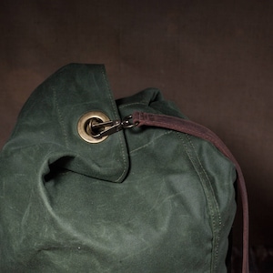 May include: A dark green canvas duffel bag with a brown leather strap and a brass buckle.