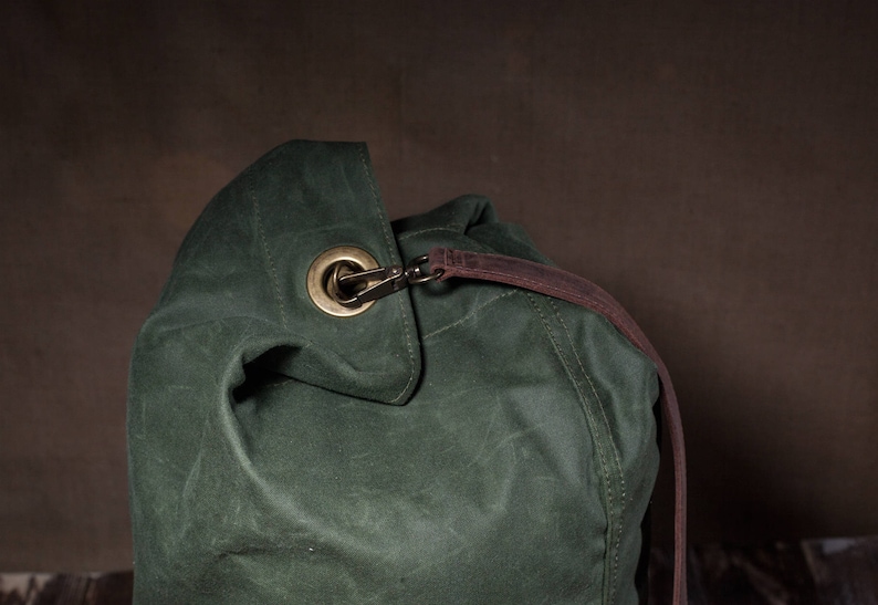 May include: A dark green canvas duffel bag with a brown leather strap and a brass buckle.